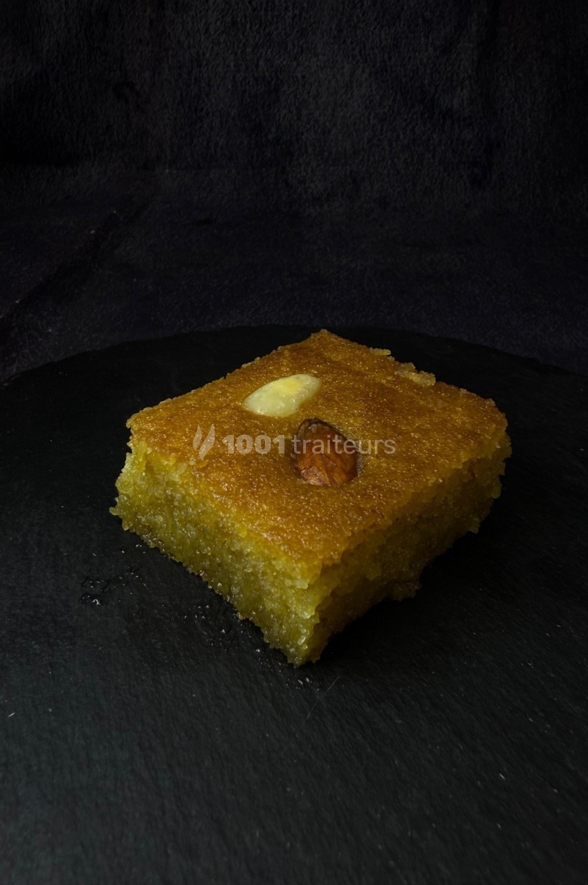 Part de gâteau de semoule doré, décorée d'une amande entière et posée sur une surface sombre.
