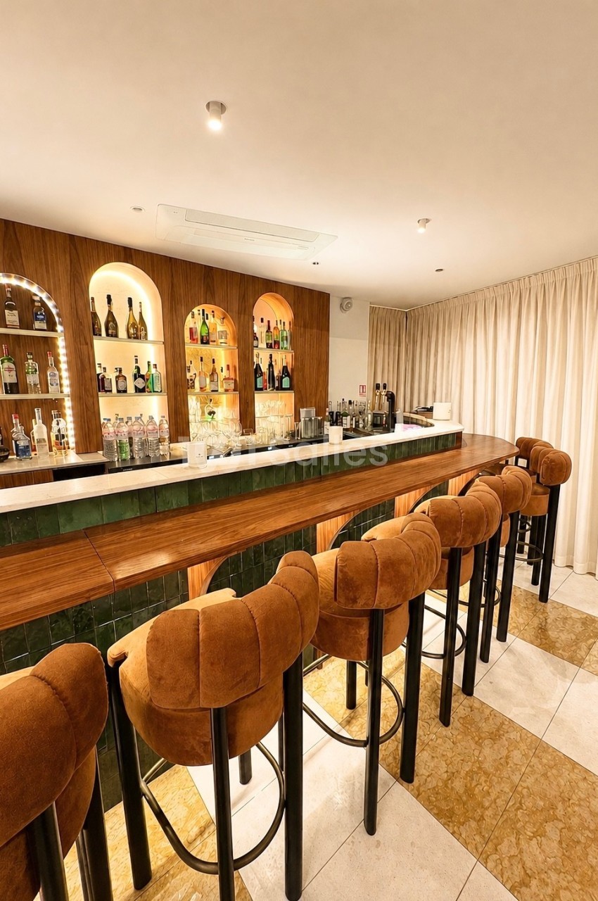 Bar élégant avec comptoir en bois, tabourets rembourrés et étagères illuminées garnies de bouteilles.