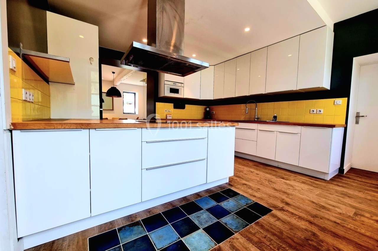 Cuisine moderne avec meubles blancs, plan de travail en bois, crédence jaune, sol en bois et carreaux décoratifs.