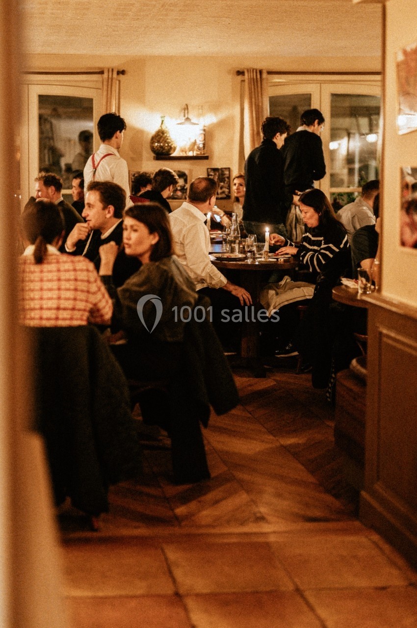 Salle de restaurant animée avec des convives attablés et des serveurs en mouvement dans une ambiance chaleureuse.