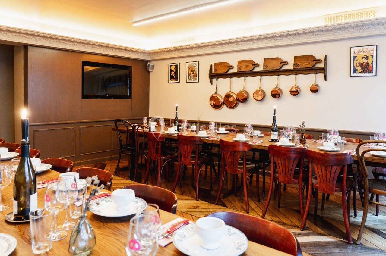 Salle de restaurant chaleureuse avec tables en bois dressées, chaises assorties et décoration murale rustique.