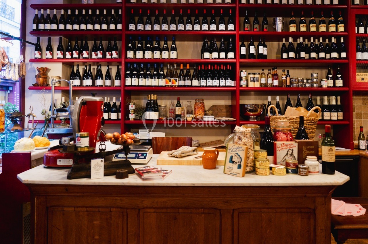 Comptoir d'une épicerie avec des produits artisanaux et des étagères remplies de bouteilles de vin en arrière-plan.