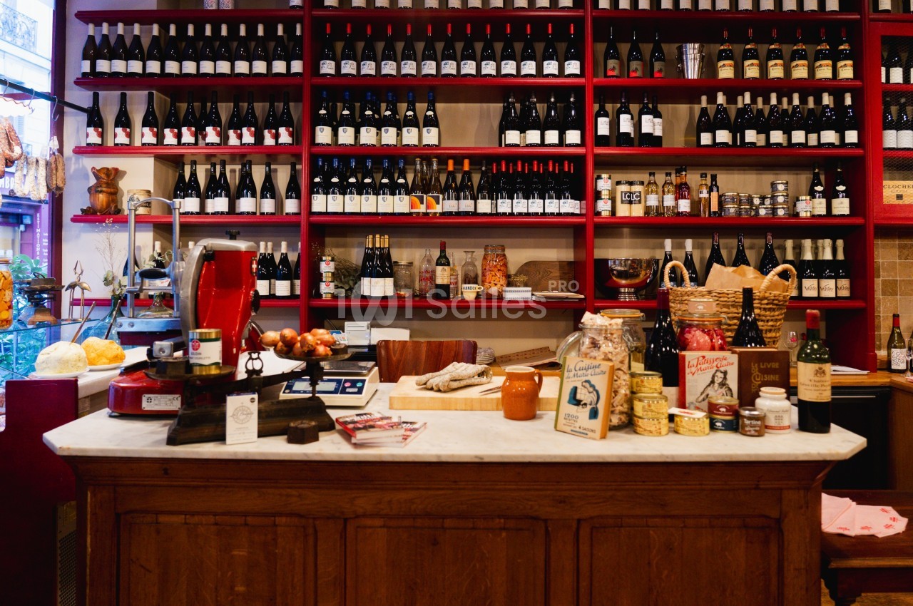 Comptoir en bois dans une épicerie avec étagères remplies de bouteilles de vin et produits artisanaux.