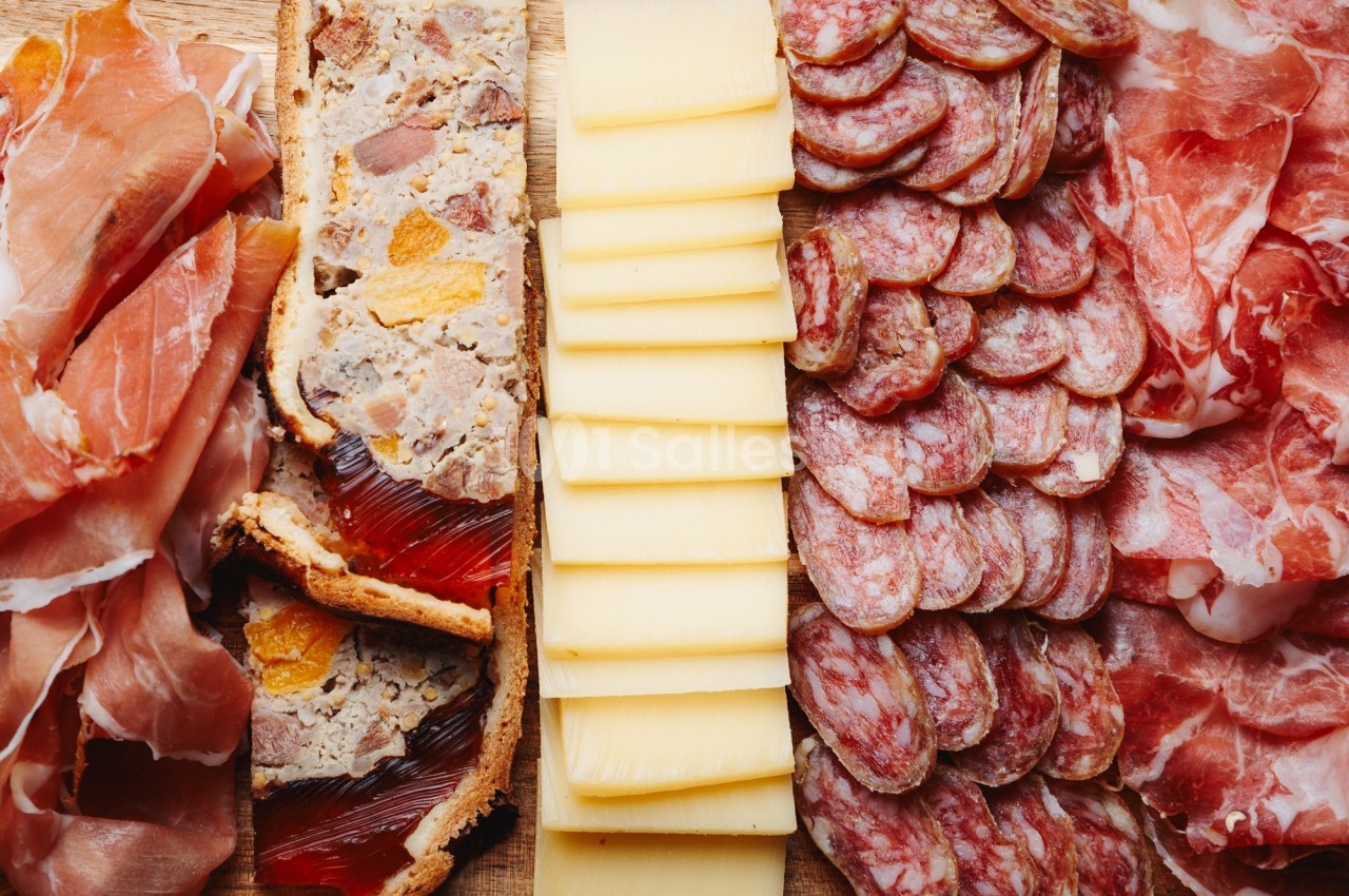 Plateau composé de jambon cru, pâté en croûte, tranches de fromage et saucisson disposés sur une planche en bois.