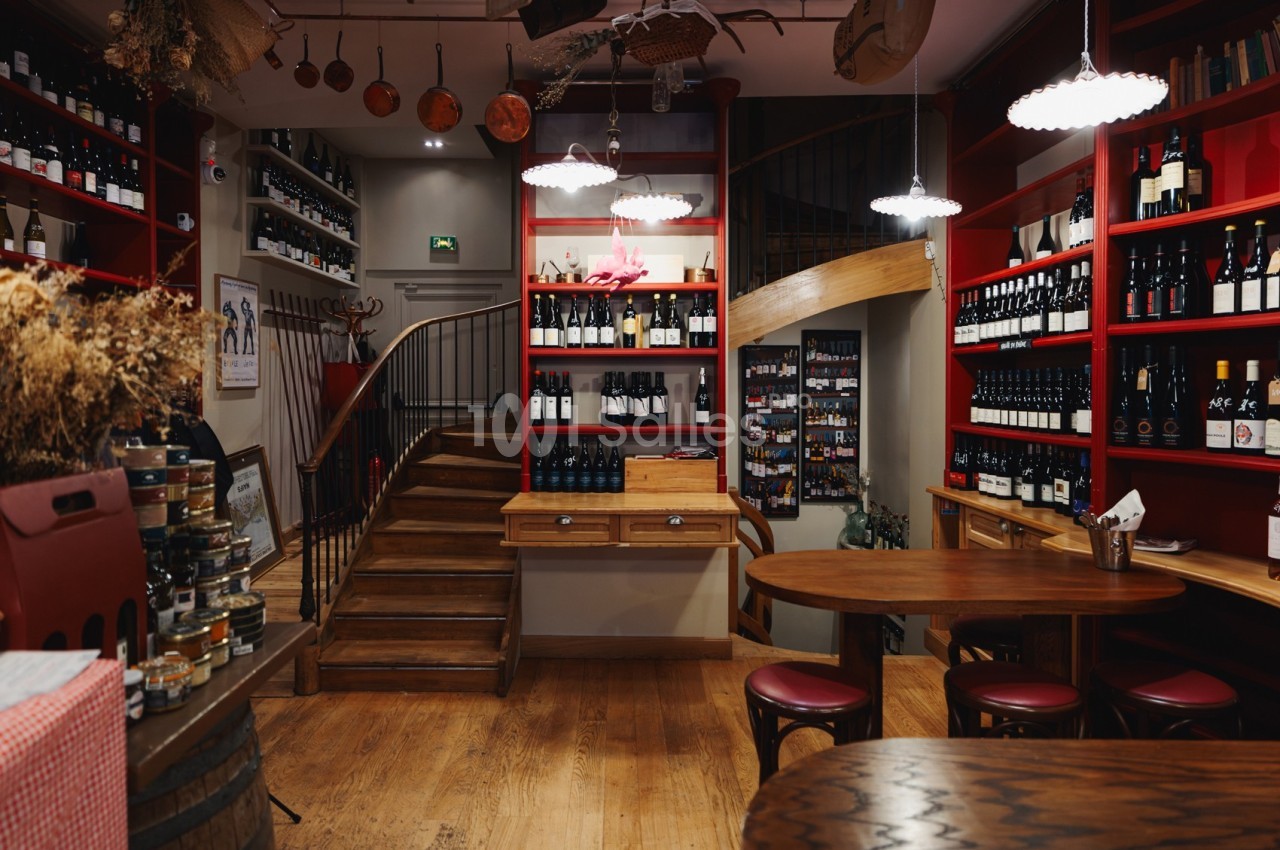 Intérieur d'une cave à vin avec étagères remplies de bouteilles, escalier en bois et tables pour dégustation.