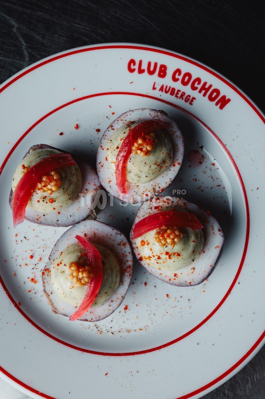 Quatre œufs mimosa garnis de crème, moutarde en grains et pickles, présentés sur une assiette blanche.