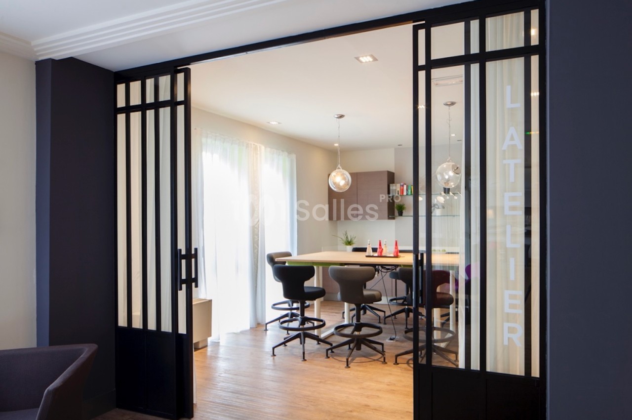 Salle de réunion moderne avec table haute, chaises noires et portes vitrées coulissantes ouvertes.