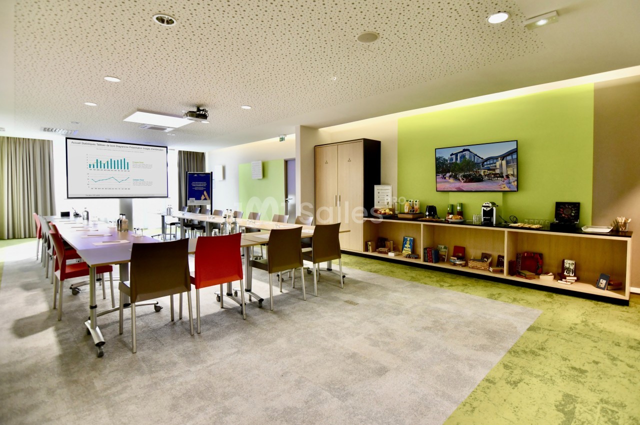 Salle de réunion moderne avec tables, chaises colorées, écran de présentation et étagères décorées.