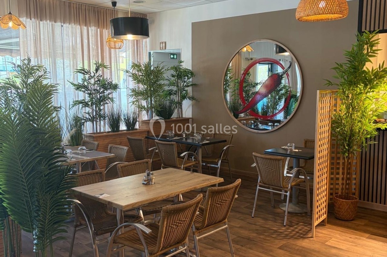 Salle de restaurant lumineuse avec tables en bois, chaises en rotin et plantes vertes décoratives.