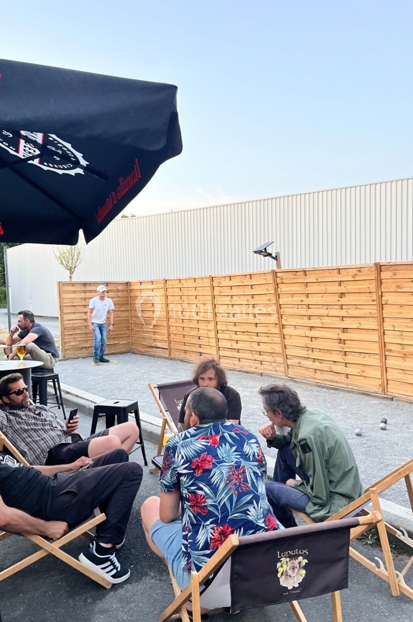 Des personnes assises sur des chaises longues discutent dans un espace extérieur près d'un terrain de pétanque.