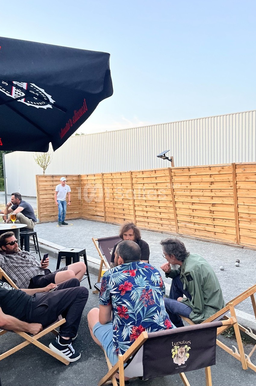 Groupe de personnes assises en extérieur sur des chaises, discutant près d'un terrain de pétanque et d'une clôture en bois.