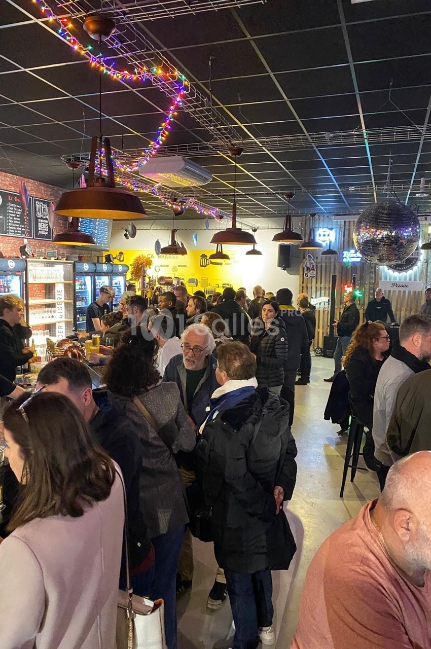 Des personnes discutent et se détendent dans un bar animé, avec des lumières colorées et un comptoir en arrière-plan.