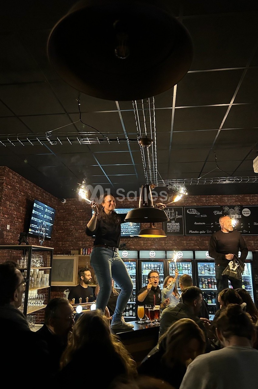 Une femme danse sur un comptoir dans un bar animé avec des clients et des lumières tamisées.