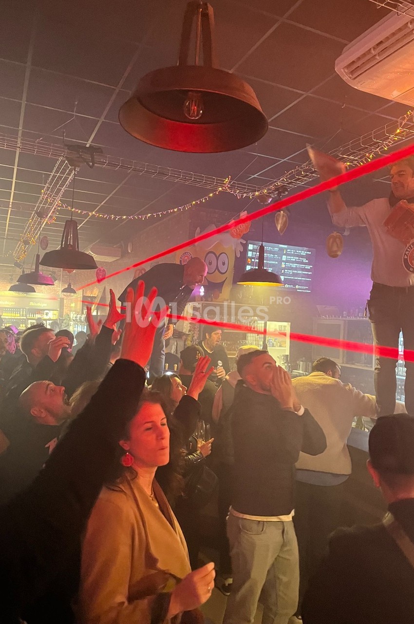 Des personnes dans un bar participent à une animation avec des lasers rouges, sous un éclairage tamisé.