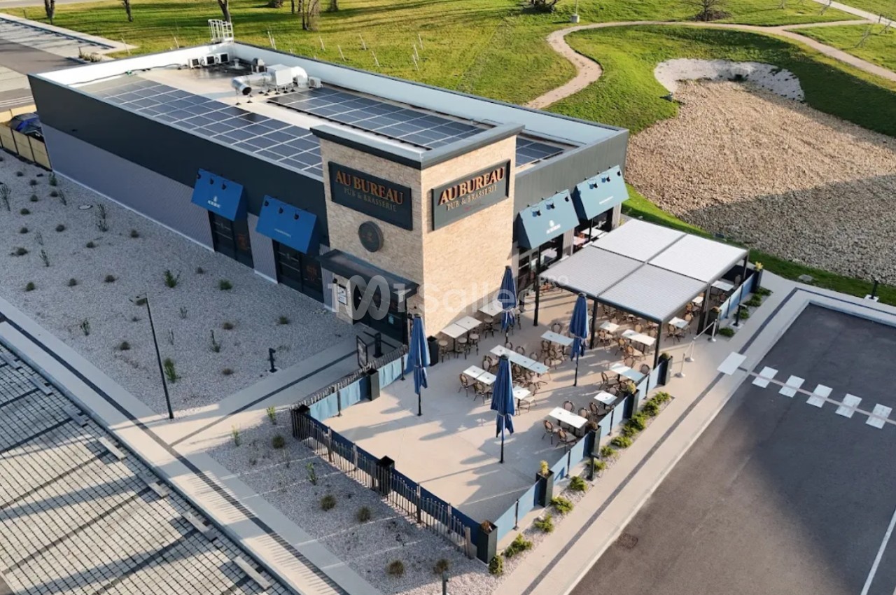 Vue aérienne d'un restaurant avec terrasse extérieure aménagée, entouré d'espaces verts et d'un parking.