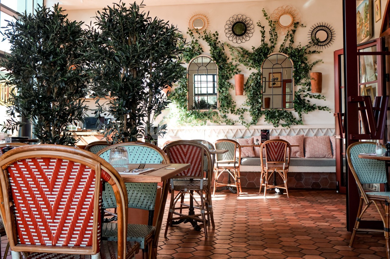 Salle de restaurant lumineuse avec des chaises en rotin, des plantes et des décorations murales en osier.