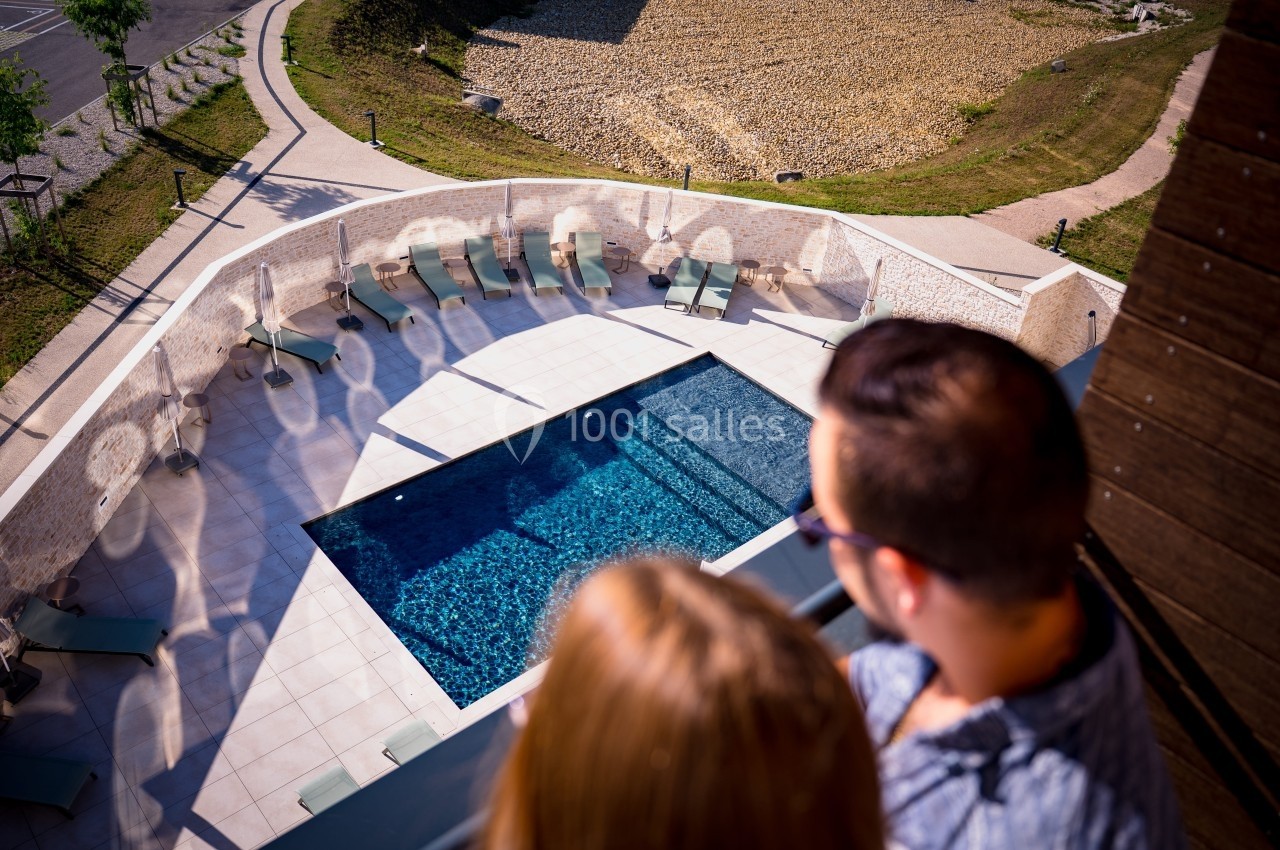 Vue plongeante sur une piscine extérieure entourée de transats, observée par deux personnes au premier plan.