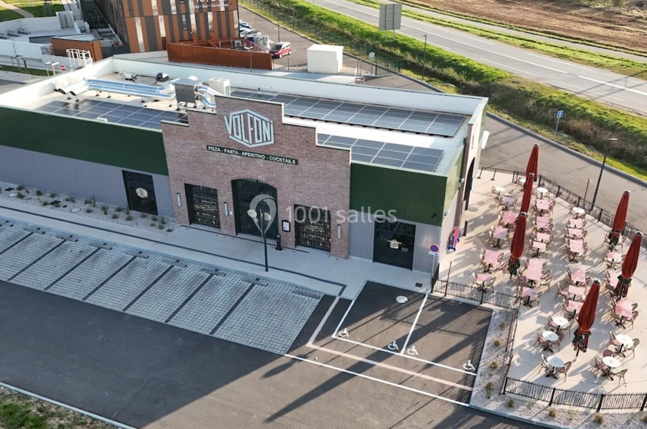 Vue aérienne d'un bâtiment commercial avec terrasse extérieure aménagée et parking adjacent.