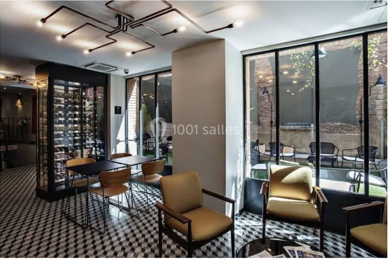 Salle lumineuse avec sol en damier, chaises modernes, vitrines de vin et grandes baies vitrées donnant sur une terrasse.