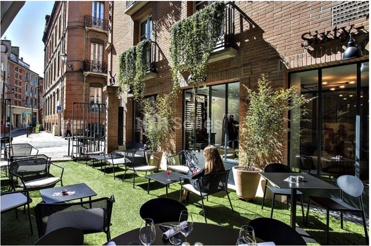 Terrasse extérieure d'un restaurant avec mobilier moderne, plantes en pots et façade en briques.