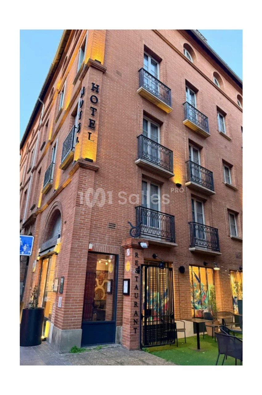 Façade en briques d'un hôtel avec balcons en fer forgé, enseignes ’Hôtel’ et ’Restaurant’, et terrasse extérieure.