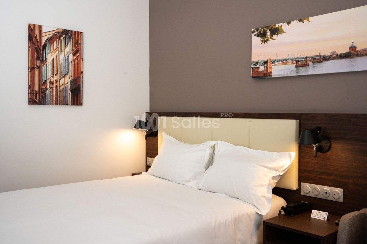 Chambre d'hôtel avec lit double, tête de lit en bois, éclairage mural et tableaux décoratifs sur les murs.