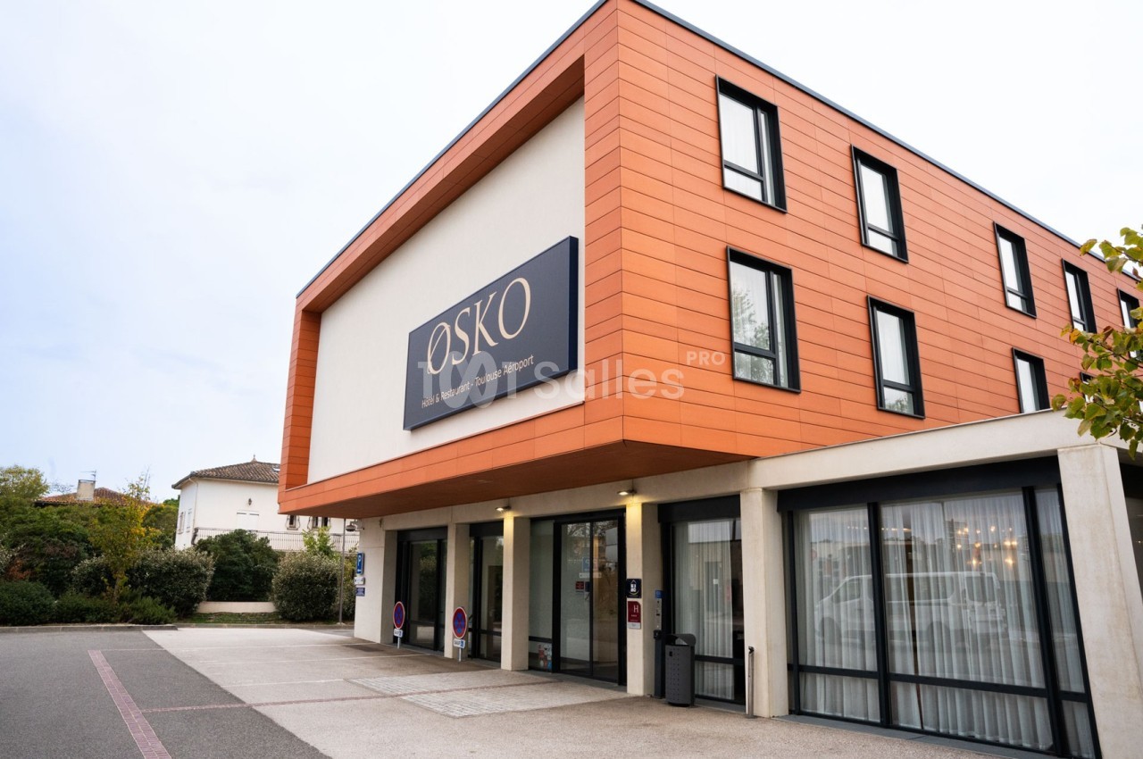 Façade d'un bâtiment moderne avec un revêtement orange, des fenêtres noires et une enseigne ’OSKO’.