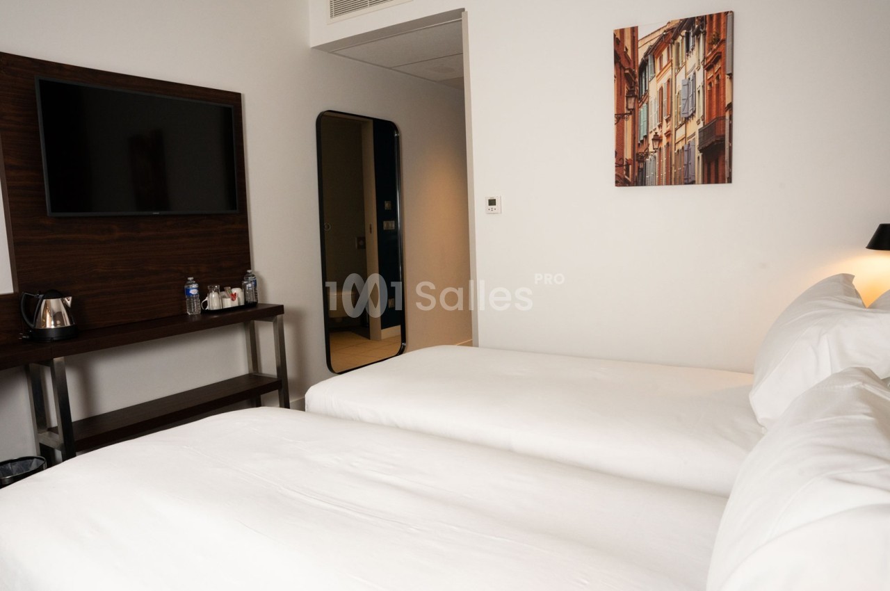 Chambre d'hôtel avec deux lits simples, une télévision murale, un miroir et une décoration murale colorée.