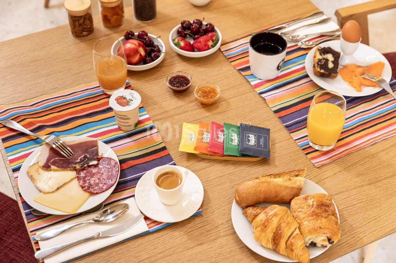 Petit-déjeuner servi sur une table avec viennoiseries, charcuterie, fromage, fruits, boissons et confitures.