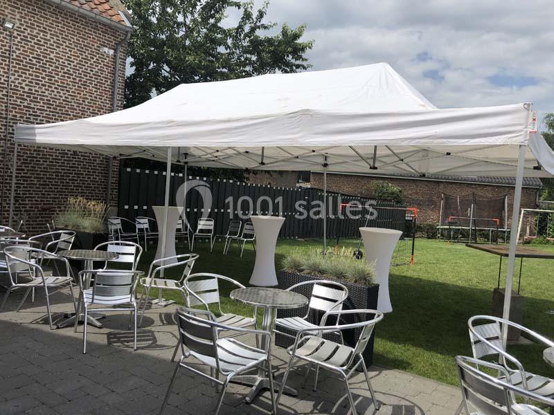 Tente blanche installée dans un jardin avec des tables et chaises en métal disposées sur une terrasse pavée.