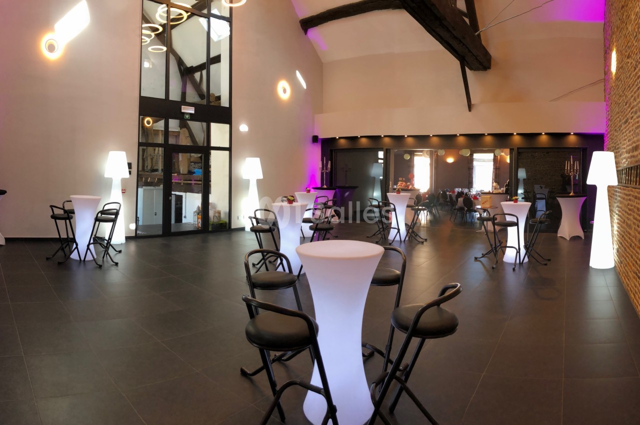 Salle de réception moderne avec murs en briques, tables hautes, chaises noires et éclairage tamisé.