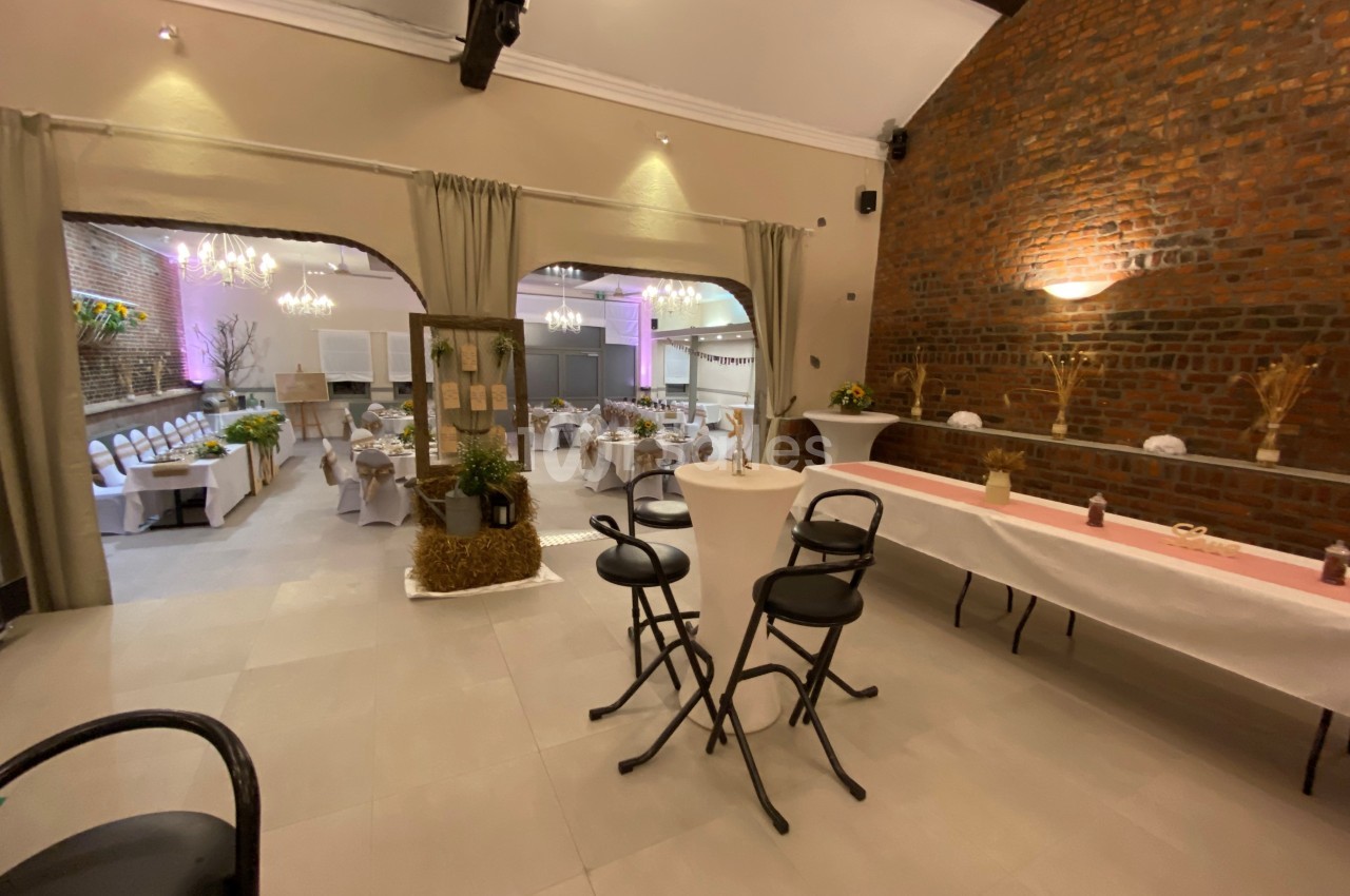 Salle de réception décorée avec des tables dressées, des chaises blanches et des éclairages chaleureux.