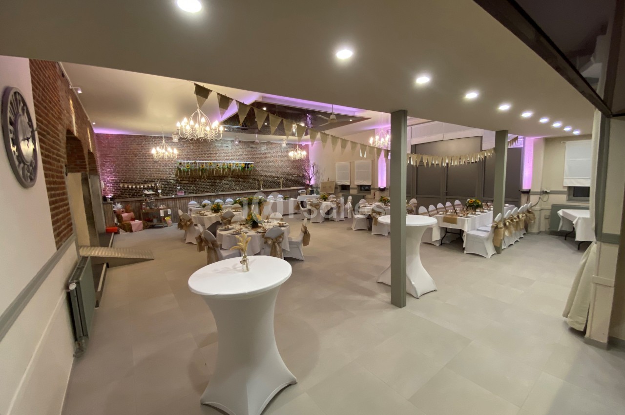 Salle de réception décorée avec des guirlandes, des tables dressées et un éclairage chaleureux.