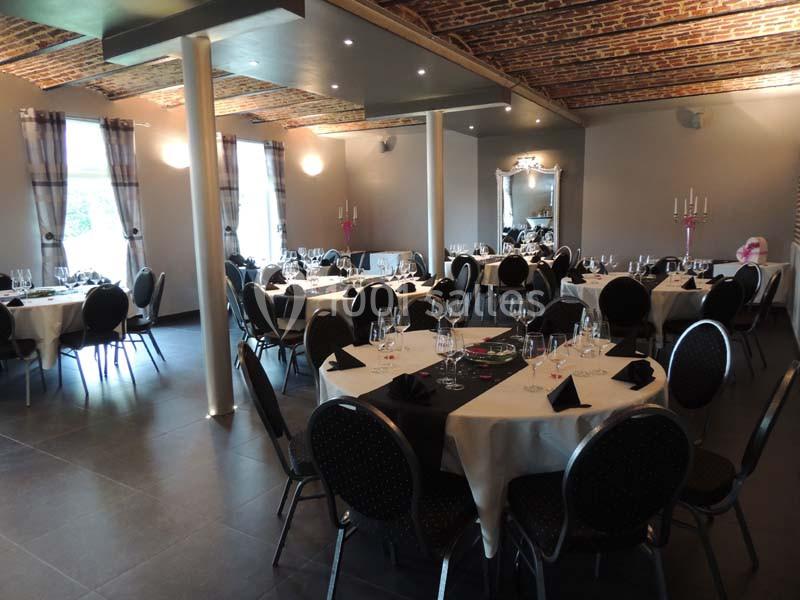 Salle de réception avec tables rondes dressées, nappes blanches, serviettes noires et chandeliers, sous un plafond en…