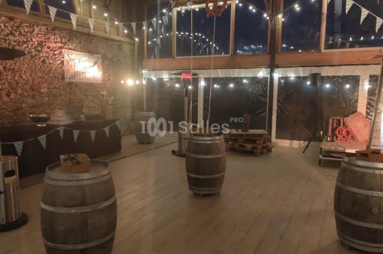 Salle décorée pour un événement, avec tonneaux en guise de tables, guirlandes lumineuses et murs en pierre apparente.