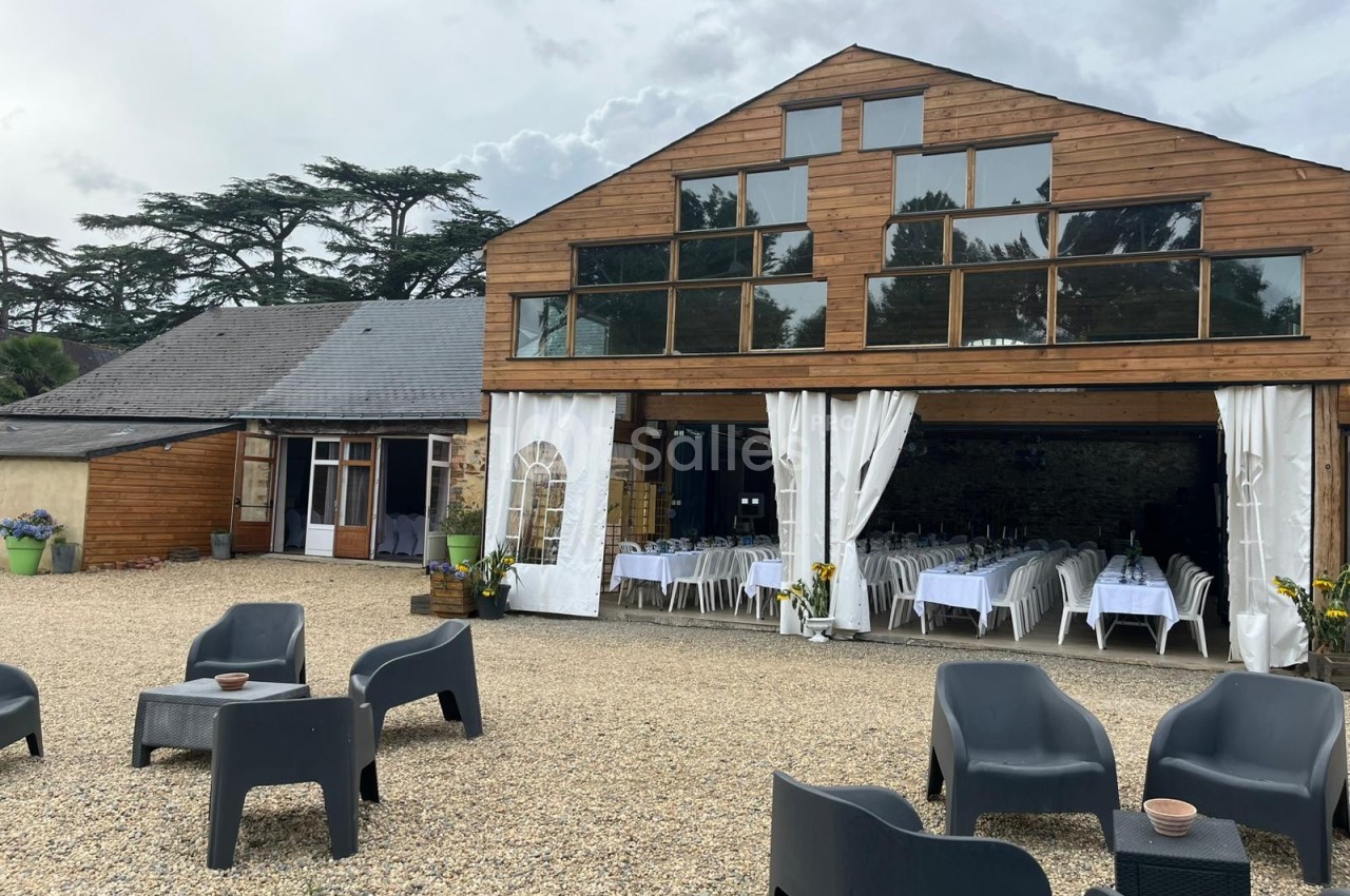 Bâtiment en bois avec grandes baies vitrées, terrasse en gravier et chaises noires, intérieur aménagé pour un événement.