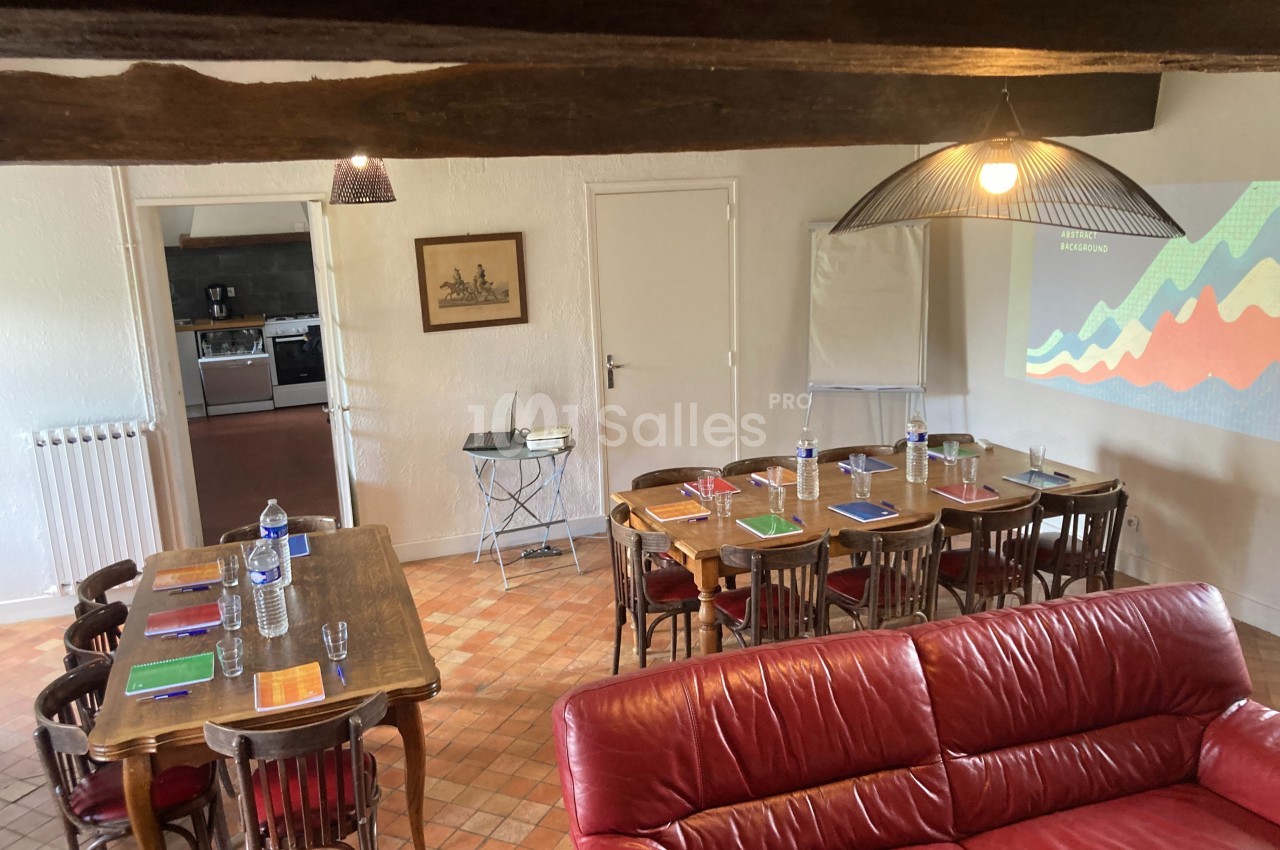 Salle de réunion avec tables en bois, chaises, écran de projection, et fournitures disposées pour une présentation.