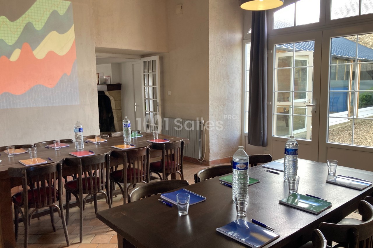 Salle de réunion lumineuse avec tables en bois, carnets, stylos et bouteilles d'eau, près de grandes fenêtres vitrées.