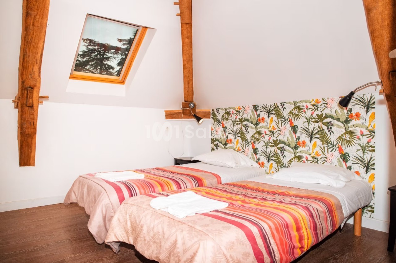 Deux lits simples avec couvre-lits colorés dans une chambre mansardée, décorée d'un mur à motifs tropicaux.