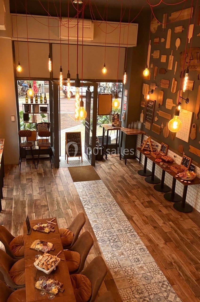 Intérieur d'un café chaleureux avec éclairage suspendu, tables en bois, sol en carrelage et vue sur l'extérieur.