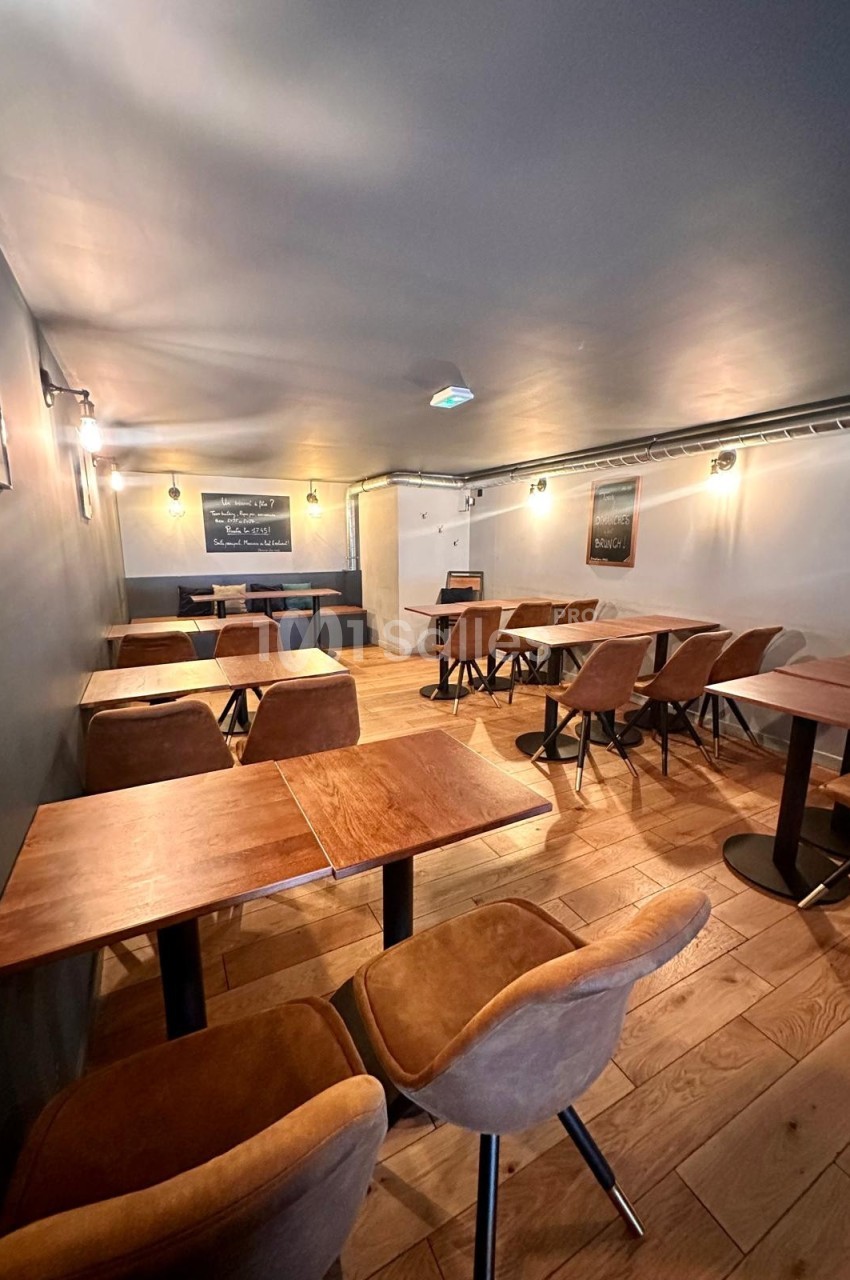 Salle de restaurant avec tables en bois, chaises rembourrées marron et éclairage tamisé sur parquet clair.