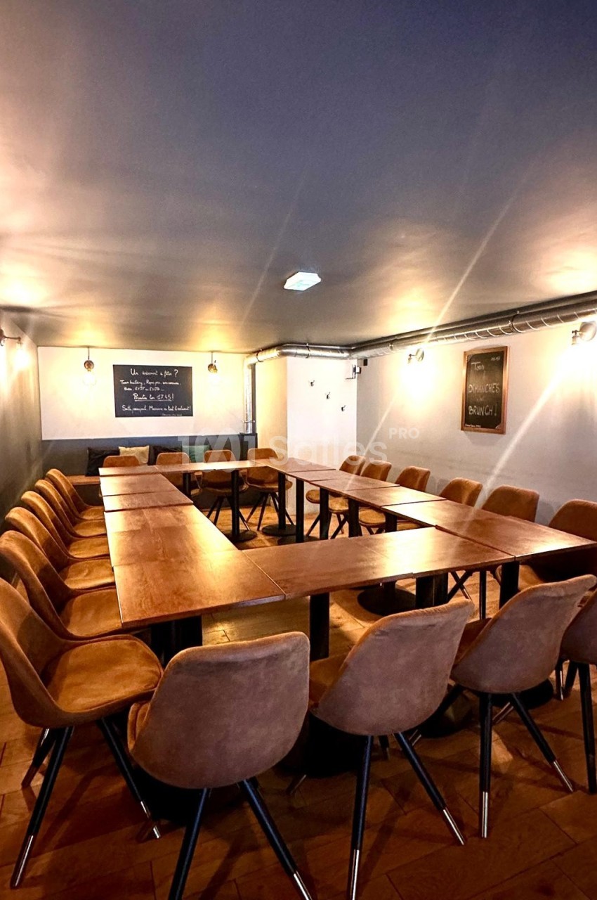 Salle de réunion avec une grande table en U entourée de chaises en cuir, éclairée par des appliques murales.