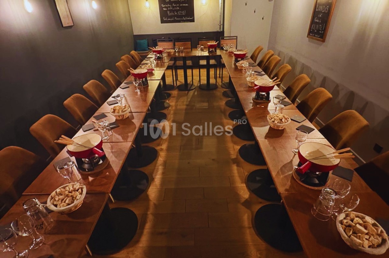 Salle de restaurant avec deux longues tables dressées pour un repas, comprenant des caquelons à fondue et des…
