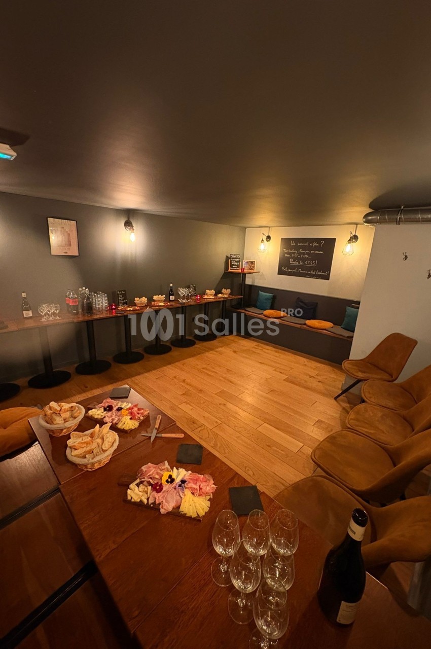 Salle conviviale avec tables dressées, planches apéritives, verres et chaises, éclairage chaleureux et décor simple.