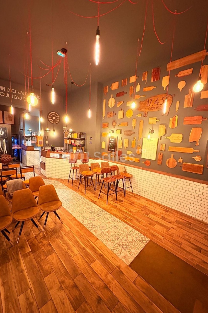 Salle de restaurant chaleureuse avec murs décorés de planches en bois, éclairage suspendu et mobilier en bois et velours.