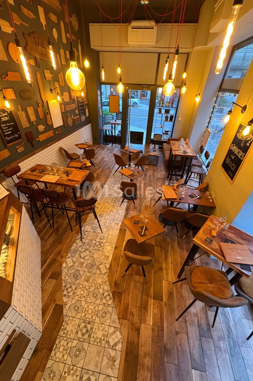 Vue d'ensemble d'un restaurant chaleureux avec tables en bois, luminaires suspendus et décoration murale éclectique.