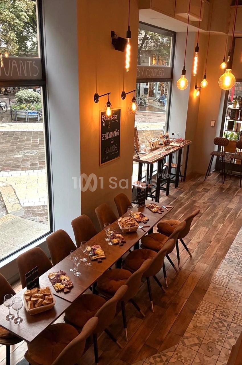Salle de restaurant lumineuse avec de grandes baies vitrées, tables dressées et planches apéritives disposées.