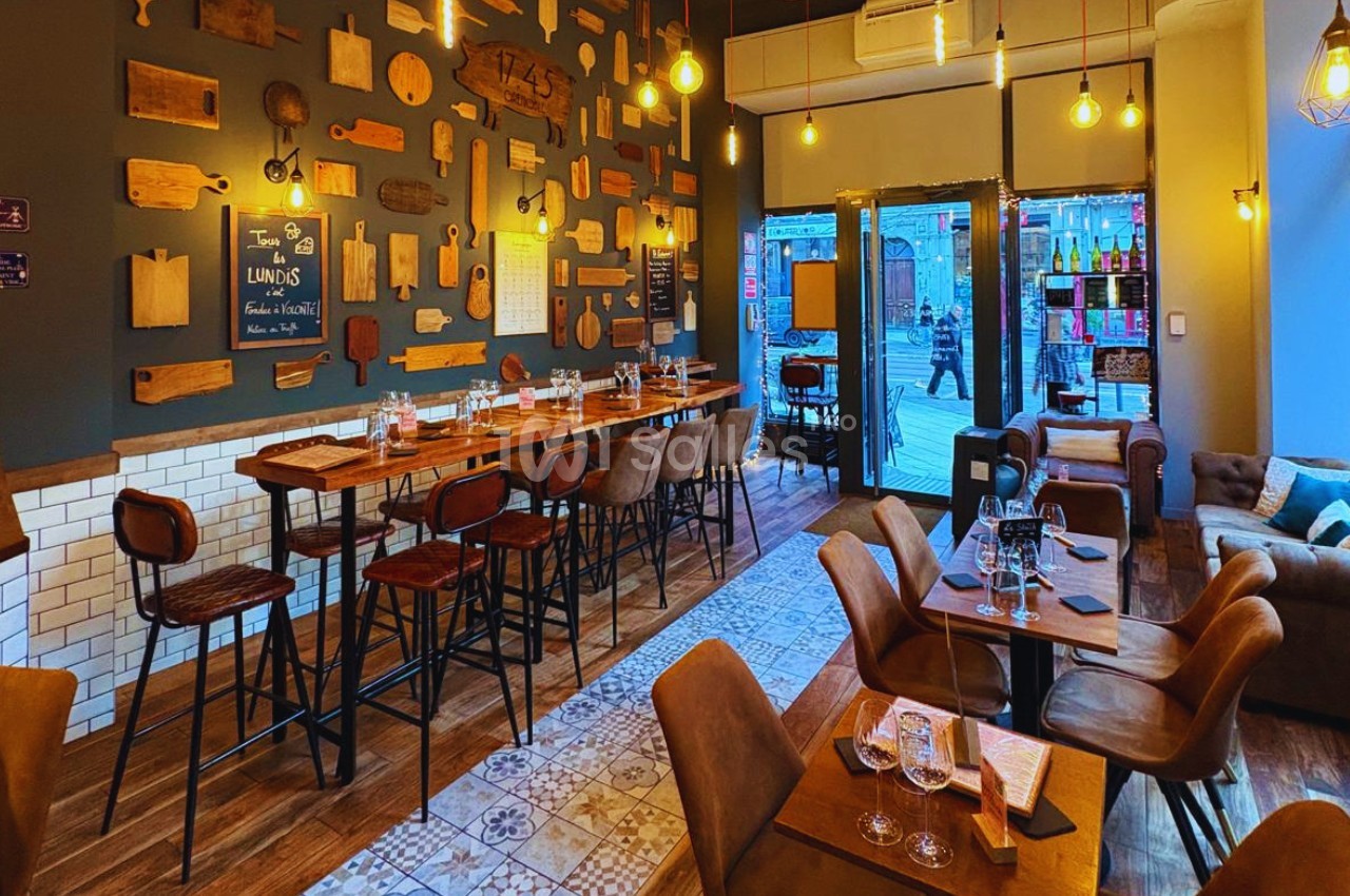 Salle de restaurant chaleureuse avec tables en bois, chaises hautes, murs décorés de planches et éclairage suspendu.