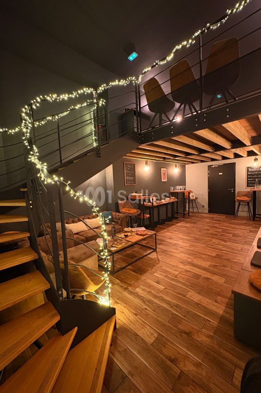 Espace intérieur chaleureux avec mezzanine, éclairage tamisé et guirlandes lumineuses, mobilier en bois et métal.