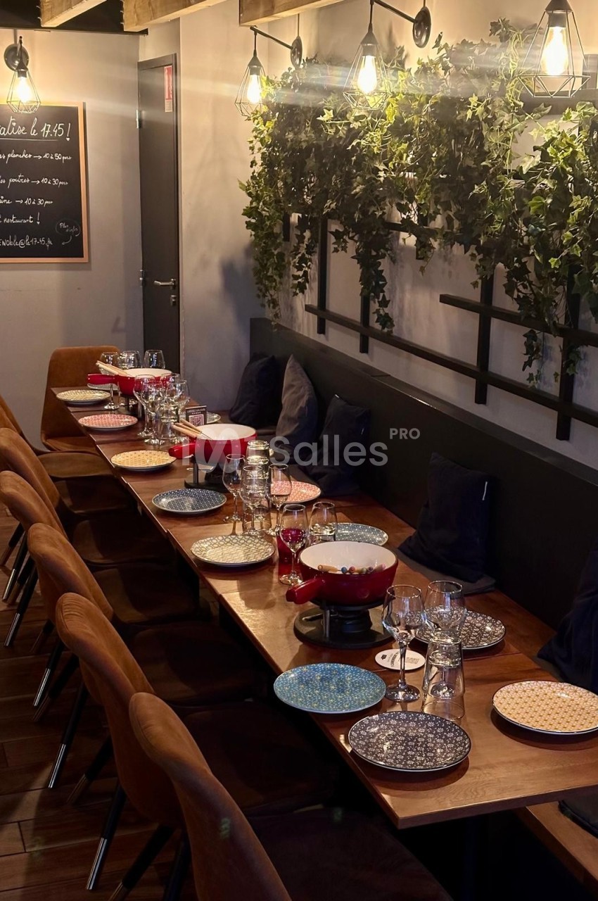 Table en bois dressée pour un repas, avec assiettes colorées, verres et fondue, dans une salle décorée de plantes murales.